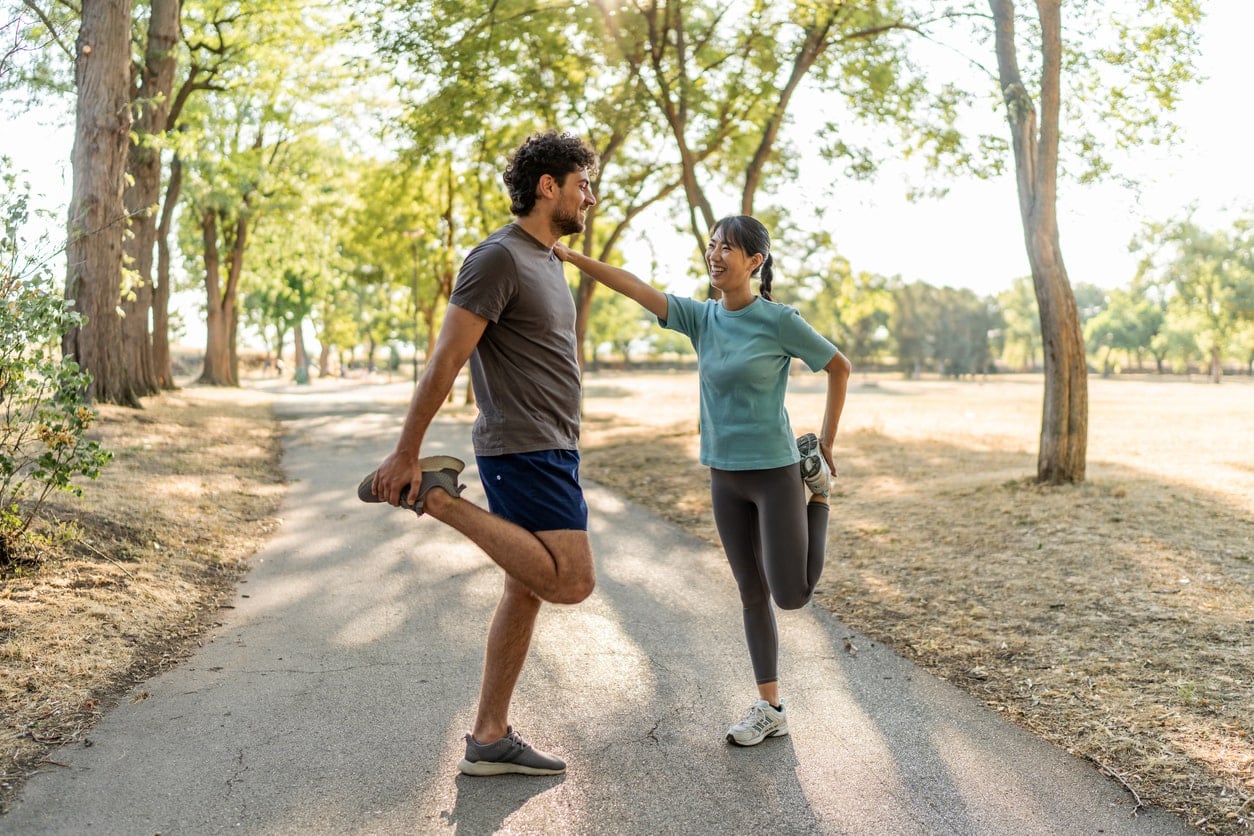 image of man and woman performing a one-legged quadriceps stretch, supporting each other for balance
